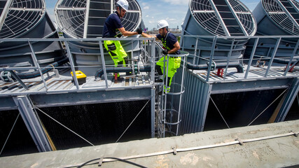 Workers perform maintenance on cooling towers at a power plant under clear blue sky