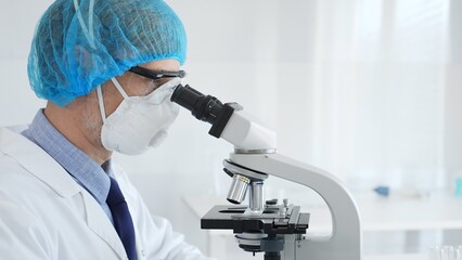 Experienced scientist examining microscopic sample, wearing full protective gear inside sterile...
