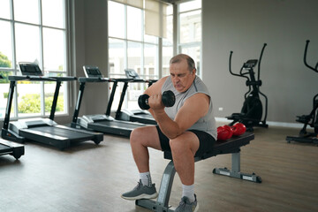 Older man lifts dumbbell in fitness center during afternoon workout session