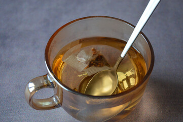 Close-up of a transparent cup with herbal tea and a tea bag steeping inside. Natural lighting and visible tea particles emphasize freshness and simplicity.