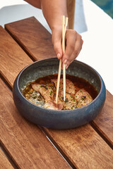 An artistic presentation of a delicious bowl of savory meat garnished with herbs, served on a wooden table, ready to be enjoyed with chopsticks.