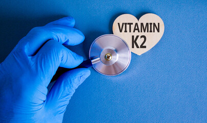 Vitamin K2 phylloquinone symbol. Concept words Vitamin K2 on wooden heart. Doctor's hand in blue...