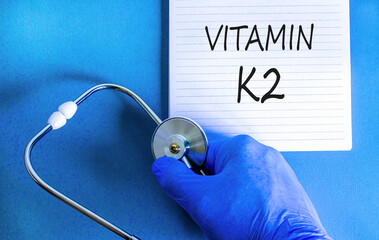 Vitamin K2 phylloquinone symbol. Concept words Vitamin K2 on beautiful note. Doctor's hand in blue...