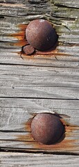 Close-up of old wooden surface with large rusty bolts and corroded metal fasteners, showing natural texture, cracks, and weathered patterns of aged timber and oxidized steel