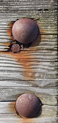 Close-up of old wooden surface with large rusty bolts and corroded metal fasteners, showing natural texture, cracks, and weathered patterns of aged timber and oxidized steel