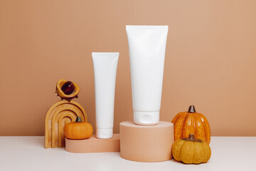 Mockup tubes of facial cream or body lotion on the brown showcase with pumpkins on brown background