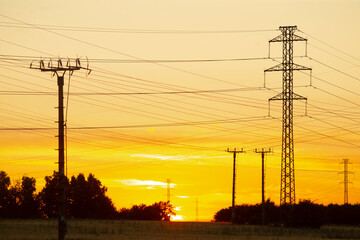 A breathtaking sunset showcases an array of power lines prominently positioned in the foreground,...