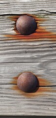 Two rusty bolts embedded in aged wooden planks with visible corrosion marks and weathered wood grain, forming a rustic industrial background