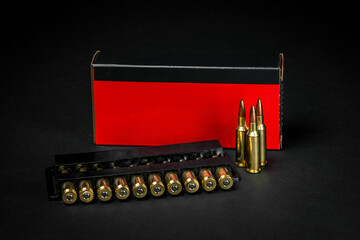 Red and black ammo box featuring a loaded stripper clip and scattered rifle rounds