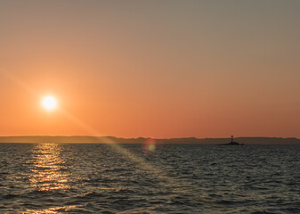 Sunset Over Ocean with Distant Lighthouse Beacon and Mountain Horizon