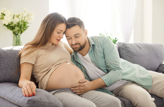 Hugging pregnant belly, loving couple sitting in hug, future parents expecting first baby close at home, caring husband and wife, expressing love, parenthood, new life, planning, dreaming, giving care