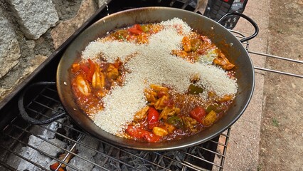 Traditional spanish paella cooking outdoors over open flame with rich ingredients. Rice in the...