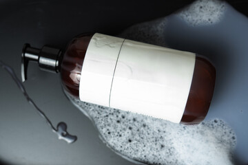 Brown dispenser bottle lying on soapy surface with blank label for mockup