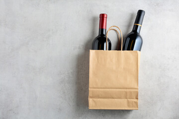 Bottles of red wine in a paper bag on a white stone background.