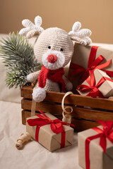 Handmade Crochet Reindeer Toy with Red Scarf Surrounded by Christmas Gifts on Wooden Background