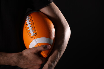 Close-up of an athlete's hand playing American football, holding a football in the air on a black background