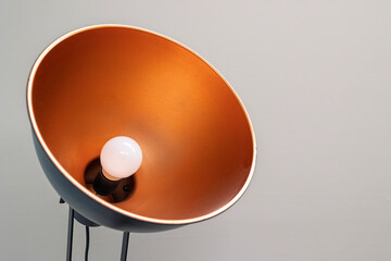 Contemporary floor lamp with a round metal shade featuring copper-colored interior and round white...