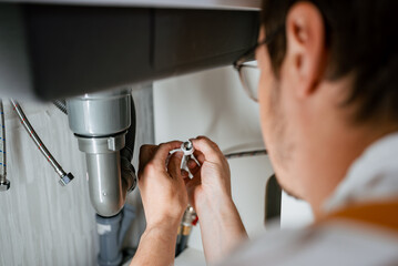 Obraz premium Professional plumber carefully connecting water pipe to the mixer, performing plumbing work under the sink, ensuring proper water flow and functionality in the kitchen or bathroom