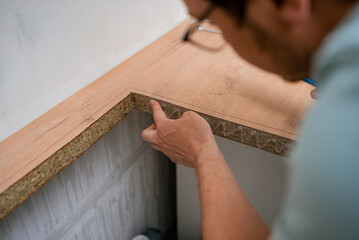 Carpenter carefully applying glue on kitchen countertop edge, preparing to install sink, demonstrating precision and expertise in home renovation
