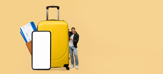 A tourist stands beside bright yellow luggage and holds a smartphone with a blank screen, excited...
