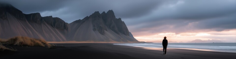 Solitary figure by dramatic mountain and ocean sunrise