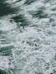 Foamy ocean waves with white sea foam creating intricate lace-like patterns across dark green water...