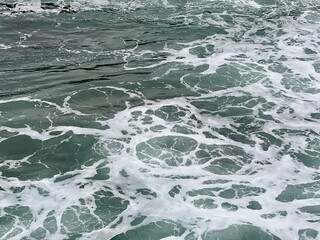 Ocean surface with white foam creating circular and flowing patterns against dark green water, resembling abstract art with organic shapes and natural water formations