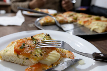 A slice of Argentine Neapolitan pizza on a plate and the rest of the pizza in the background out of focus