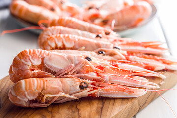 Scampi langoustine on cutting board on white table.