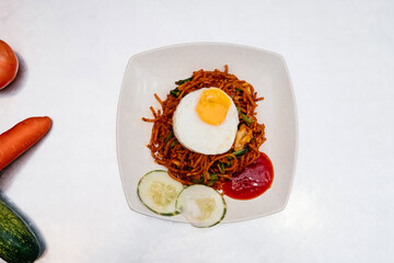 Spicy Chicken Mee Goreng with Fried Egg, Cucumber, and Sauce on a White Plate isolated on white background top view of Malaysian food