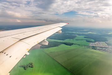 View of airplane wing, blue skies and green land during landing. Airplane window view.