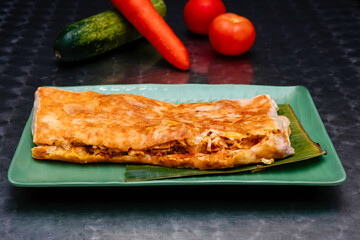 Chicken Murtabak on a Banana Leaf Garnish on a Plate isolated on dark background side view of Malaysian food