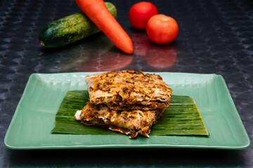 Mutton Murtabak sliced half on a Banana Leaf Garnish on a Plate isolated on dark background side...