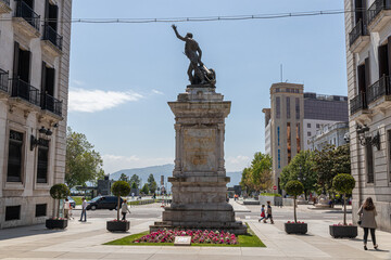 Santander, Spain. Full view of the bronze statue of Captain Pedro Velarde on a stone pedestal at the entrance to Plaza Porticada, with Neoclassical portico and surrounding arcaded buildings