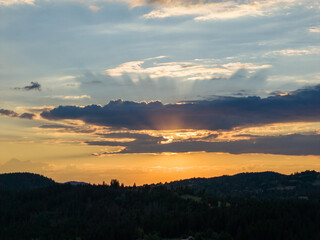 Fototapeta premium Warm sunset light breaks through layered clouds, casting golden tones across distant forested hills and valleys