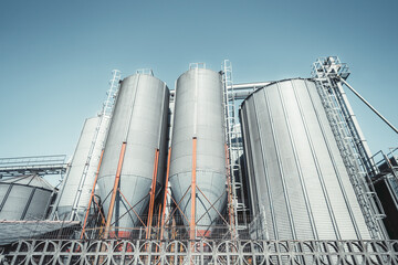 Modern agricultural silos made of corrugated metal under clear blue sky, used for storing grain or...