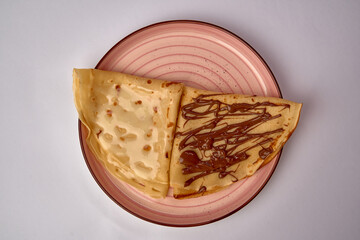 Deliciously Prepared Crepes Served on a Pink Decorative Plate, Half Plain and Half Spread with Rich Chocolate Sauce for a Sweet Treat.
