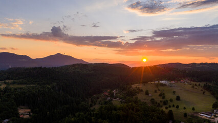 A wide-angle view of sunset illuminating a layered mountain landscape with forested valleys and rural scenery