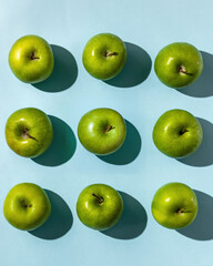 Top view of nine fresh green apples arranged in three rows on a solid blue background. Clean minimalist composition with shadows, ideal for design, advertising, and healthy food themes.