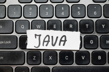 Handwritten note reading JAVA placed on a black computer keyboard. Java is a popular programming...