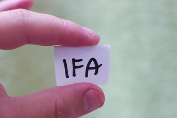 A hand holding a small paper with the handwritten letters IFA, symbolizing identity, organization,...
