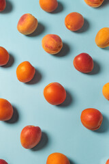 Scattered fresh apricots on pastel blue background. Minimalist summer concept with vibrant colors. Ideal for themes of health, nature, food, freshness, and organic lifestyle.