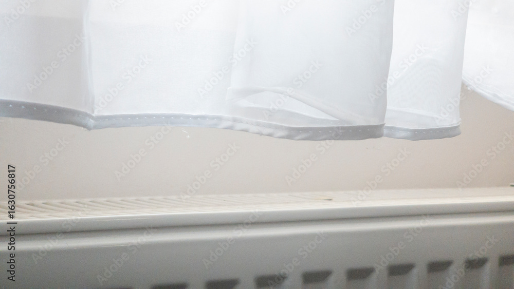 Poster a sheer white curtain gently drapes over a radiator in a softly lit room, creating a serene atmosphe