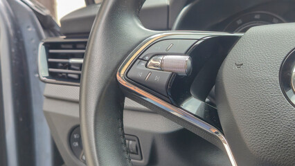Close-up view of a modern car steering wheel featuring control buttons for audio and settings,...