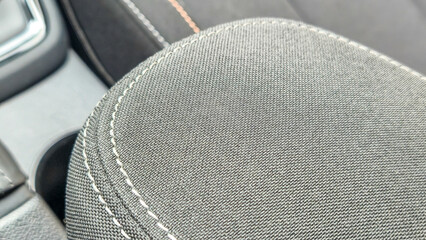 Close-up view of a car armrest with textured black fabric and visible stitching details, showcasing...
