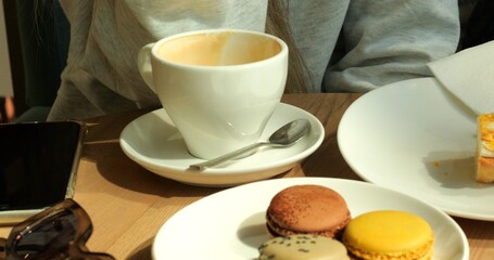Richly brewed coffee accompanied by macarons and decadent slice of pastry. Mobile phone and chic sunglasses complete scene of sweet indulgence