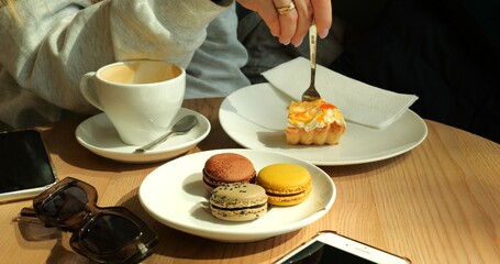 Woman relishes sumptuous slice of pastry indulging in flavors of macarons. Smartphone and sleek...