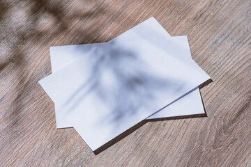 Minimalistic white mockup of a blank postcard lying on a wooden surface with soft natural shadows...