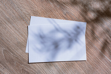 Minimalistic white mockup of a blank postcard lying on a wooden surface with soft natural shadows...