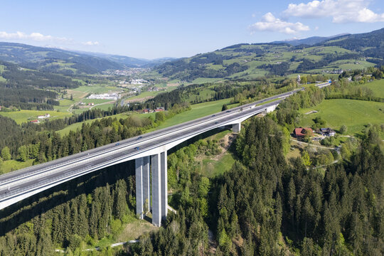 Aerial view of a long bridge cutting through lush green hills and valleys, its concrete pillars contrasting with the dense forest, Wolfsberg, Carinthia, Austria.